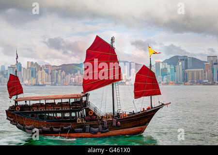 HDR rendering of a typical Chinese junk ship with red sails on Victoria Harbor in Tsim Sha Tsui, Hong Kong. The emerald-colored  Stock Photo