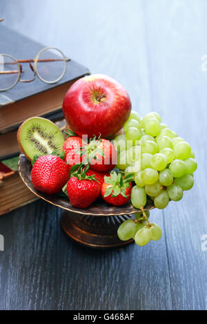 Nice metal bowl full of various fruits on wooden table near old books Stock Photo