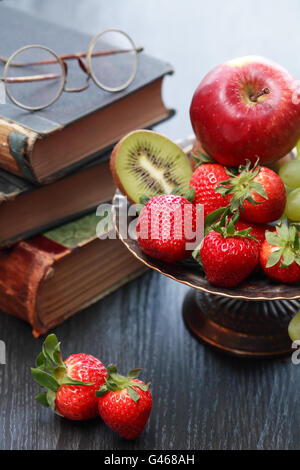 Nice metal bowl full of various fruits on wooden table near old books Stock Photo