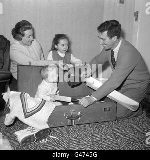 Nine month old Mark Titmus offers his own miniature bat as he joins the family in helping his father, Middlesex and England cricketer Fred Titmus, to pack at home for the MCC tour of India and Pakistan. Also pictured are his wife Jean and six year old daughter Dawn. Stock Photo