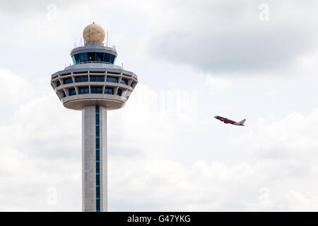 Singapore Changi International Airport traffic controller tower with airplane taking off in the background. Stock Photo
