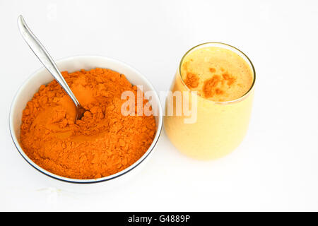 Turmeric and ginger smoothie milkshake in stemless glass with bowl of powdered turmeric next to glass, isolated on white Stock Photo
