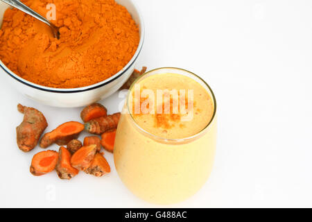 Turmeric Smoothie and turmeric powder in bowl with spoon and pieces of turmeric root isolated on white. Horizontal photo. Stock Photo