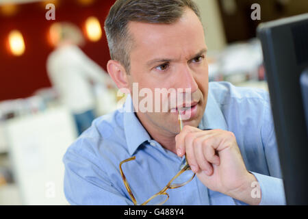 Man working on computer, arm of spectables in his mouth Stock Photo
