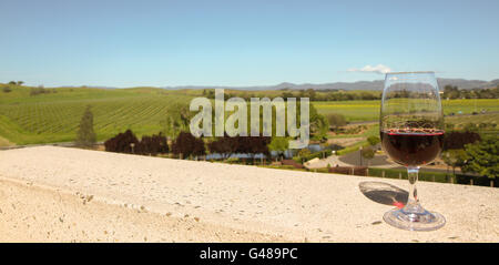 Glass of red wine on balcony overlooking Nap Valley Wine Country California. Green trees, small pond and vineyards in mid-ground Stock Photo