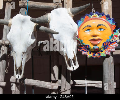 Bleached Cattle Skull and Painted Ceramic Sun, Santa Fe, New Mexico. Closeup photo, skull is hanging on an adobe colored wall. Stock Photo