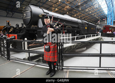 Highland piper Colin Sutherland plays in front of the Flying Scotsman in its wartime LNER black livery on display on the turntable at the National Railway Museum, York. Stock Photo