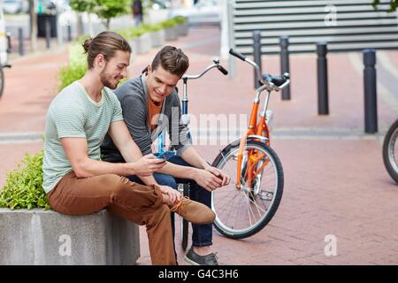 MODEL RELEASED. Two young men sitting on wall with smartphone. Stock Photo