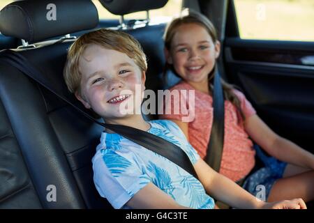 MODEL RELEASED. Brother and sister in the back seat of the car wearing seat belts. Stock Photo