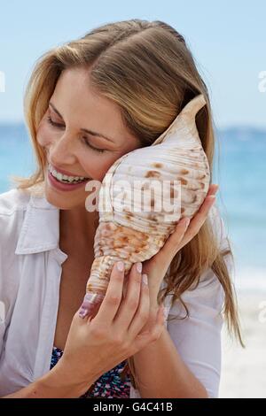 MODEL RELEASED. Woman listening to a seashell. Stock Photo