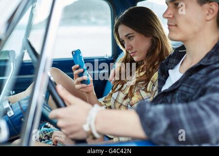 MODEL RELEASED. Young couple in a car, woman using smartphone. Stock Photo