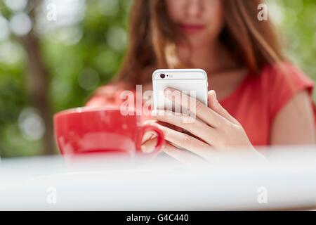 MODEL RELEASED. Young woman using smartphone with coffee, close up. Stock Photo
