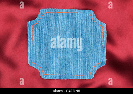 Frame for the text from a blue jeans fabric with the stitched lines of an orange thread, on a red silk Stock Photo