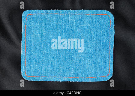 Frame for the text from a blue jeans fabric with the stitched lines of an orange thread, on a black silk Stock Photo