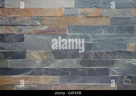 Roughly textured stone cladding tiled wall in grey and ochre colours background Stock Photo