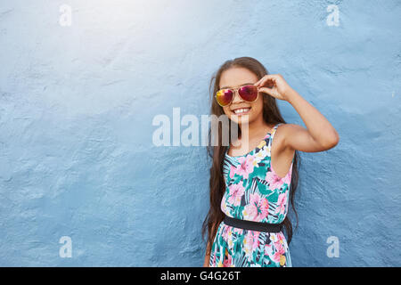 Portrait of stylish little girl with sunglasses. Preteen girl posing against blue wall with copy space. Stock Photo