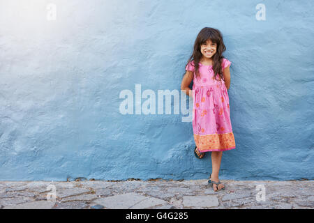Full length portrait of cute little girl smiling while standing against blue wall with copy space Stock Photo