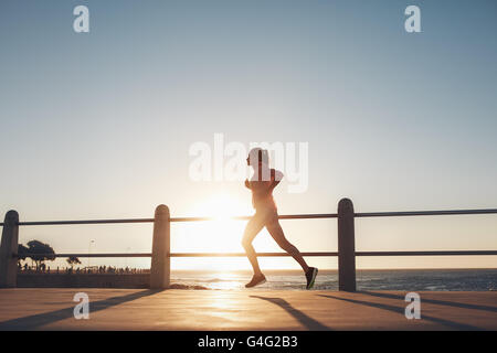 Silhouette of young woman running along the sea during sunset. fitness woman jogging on a road by the sea. Stock Photo