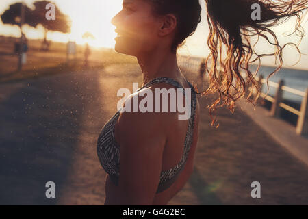Close up image of fitness woman standing outdoors during evening. She is relaxing after her workout session, with bright sunligh Stock Photo