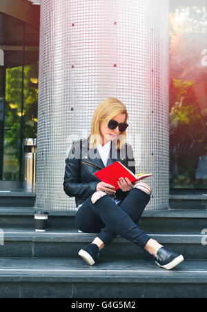 young hipster girl reading a red  book sitting on stairs Stock Photo