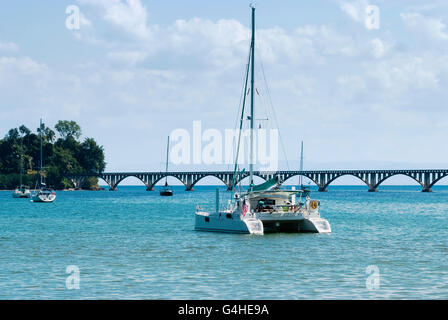 View of a catamaran and sail boats ancored at Samana Bay and  Los Puentes bridge at the background, Samana, Dominican Republic. Stock Photo