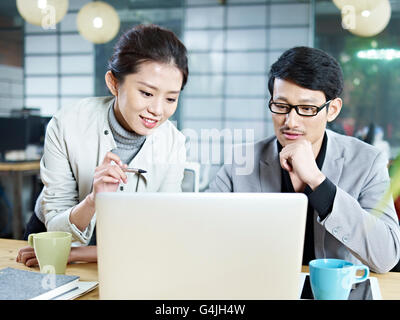 two young asian corporate people discussing business in office using laptop computer. Stock Photo