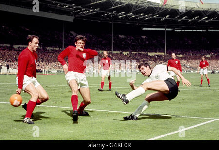 PA NEWS PHOTO 30/7/66 A LIBRARY FILE PICTURE OF ENGLAND AND WEST GERMANY IN ACTION DURING THE 1966 WORLD CUP FINAL AT WEMBLEY IN LONDON. ENGLAND WON THE MARTCH 4-2. FROM LEFT TO RIGHT: GEORGE COHEN, MARTIN PETERS OF ENGLAND AND WEST GERMANY'S EMMERICH HAVING A SHOT AT GOAL Stock Photo