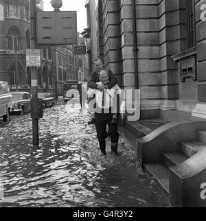 An office worker gives a colleague a piggy-back as they paddle through the flooded streets on Hull. Exceptionally high tides, 4ft 2inches above the predicted, caused the Humber to over flow. Many parked cars were surrounded by water. Stock Photo