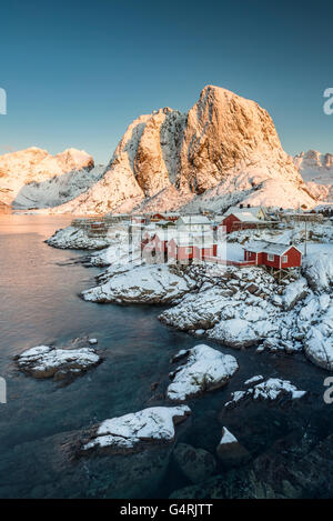Town and fisherman's cabins or Rorbus in front of snowy mountains, winter, Sakrisøya, Moskenesøy, Lofoten, Norway Stock Photo