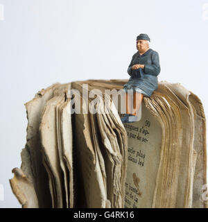 Elderly lady, miniature figurine, sitting on an old book Stock Photo