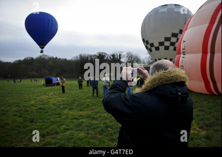 Photo. A man takes a photograph as hot air balloons take flight at the 40th Annual International Icicle Balloon Meet, on the first full weekend in January and attended by pilots and balloon crews from all over the world, gathering in a field near Savernake Forrest, near Marlborough, to take flight across the Wiltshire countryside. Stock Photo