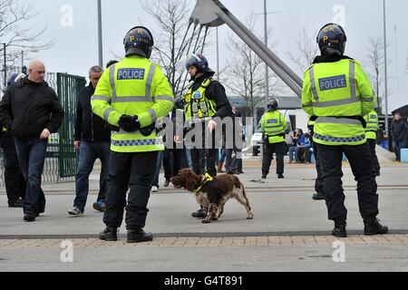 Soccer - FA Cup - Third Round - Manchester City v Manchester United - Etihad Stadium. Police officers accompanied by a sniffer dog watch as fans pass by outside the ground, before the game Stock Photo