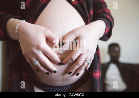 A pregnant woman is holding her baby bump. Father-to-be is sitting in the background; expectant parents. Stock Photo