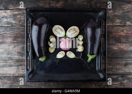 Whole and sliced eggplants arranged on rustic baking tray. Top view with copy space Stock Photo
