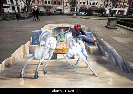 3D artist Rick Cook puts the finishing touches to his latest artwork showing a chariot with horses seemingly rearing up from out of the ground at Golden Square, Soho, London. Stock Photo