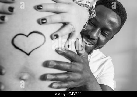 Smiling dad-to-be and his pregnant partner are holding hands over belly Stock Photo