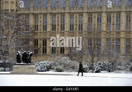 A man walks towards the Burghers of Calais statue commemorating an episode during the Hundred Years' War between England and France by Auguste Rodin, next to the House of Lords in Victoria Tower Gardens, London, following overnight snow. Stock Photo