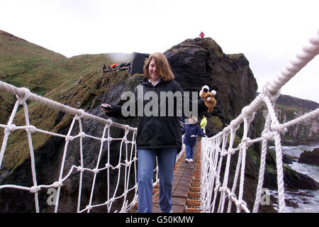 Tourists cross the new National Trust rope bridge at Carric-a-rede on the North Antrim coast in Northern Ireland. The 50,000 bridge spans a spectular 80 foot spasm between the mainland and Carric-a-rede rock, a Salmon fishery for a least 350 years. * Up to 100,000 people visit the site over the year as well as the local fishermen who still use the rock. The old bridge had to be replaced after a health and safety report. Stock Photo