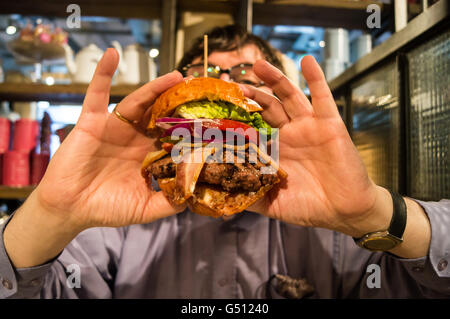 A man preparing to bite into BLT hamburger with lettuce, tomato, red onion, horseradish and  mayo, Bill's restaurant, Clink Street, London mrd mrhd Stock Photo