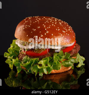 Juicy, tasty burger with pickles, tomatoes and onions on a black background Stock Photo