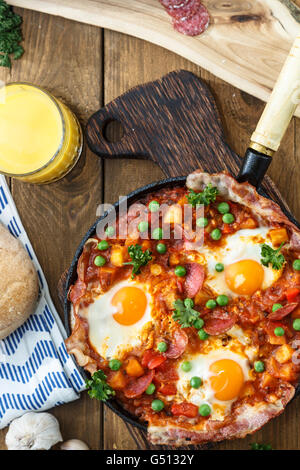 baked eggs with chorizo, potatoes and tomatoes in a pan on the table. top view Stock Photo