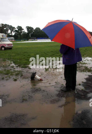 A spectator looks out from underneath his umbrella at the waterlogged pitch, as rain delays the start of the Benson & Hedges Cup semi-final between Glamorgan and Surrey, at Glamorgan's Sophia Gardens ground, in Cardiff. Stock Photo