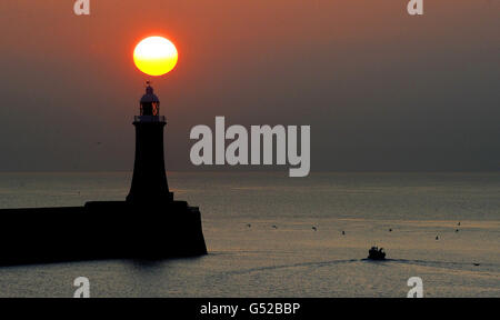 The sun rises over the lighthouse on Tynemouth Pier, Tyne and Wear as a fishing boat goes out to sea. Stock Photo