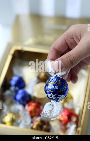 Close up of hand holding blue wrapped Lindt Lindor Chocolate with gold colour box in the background Stock Photo