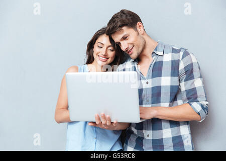 Portrait of happy young couple using laptop isolated on gray background Stock Photo