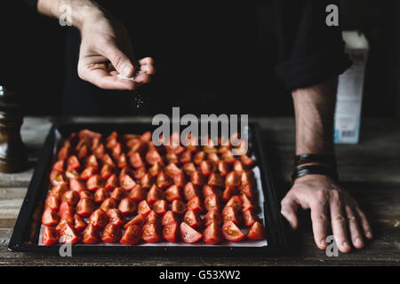 Male chef salting down tomatoes on a tray. Preparing cherry tomatoes for roasting Stock Photo