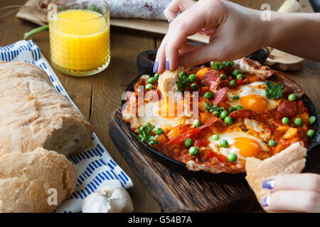 Hand dip bread into flamenco eggs or huevos a la flamenca, andalusian cuisine Stock Photo