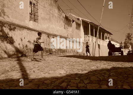 Two boys running towards each other on a cobbled street in Trinidad Cuba with a man on a wooden cart Stock Photo