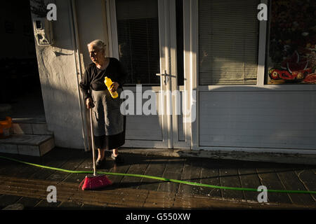 An elderly woman cleans the sidewalk outside her shop in the village of Anogia, on the island of Crete in Greece Stock Photo