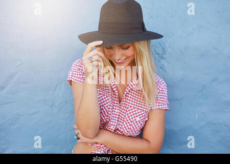 Portrait of smiling young woman with hat against blue wall. Attractive female model looking happy. Stock Photo